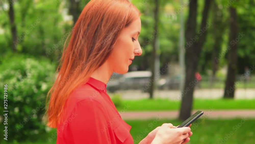 Young Girl Walking Along The Street And Chatting With Friend On Phone. Green Trees Around. Relaxing Timespending. Young Girl Walking Along The Street And Chatting With Friend On Phone. Green Trees Around. Relaxing Timespending.