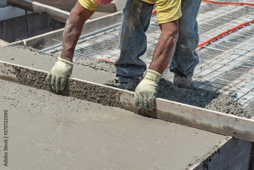 Worker levels a floor cement mortar. Using a straight wooden board to level a rooftop Worker levels a floor cement mortar. Using a straight wooden board to level a rooftop
