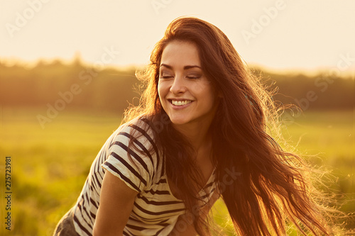Beautiful laughing young woman with closed eyes and amazing bright long hair on nature bright sunset summer background. Closeup