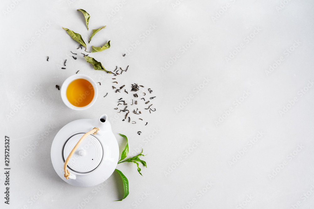 Tea concept with white tea set of cups and teapot surrounded with fresh tea leaves on concrete background with copy space. - obrazy, fototapety, plakaty 