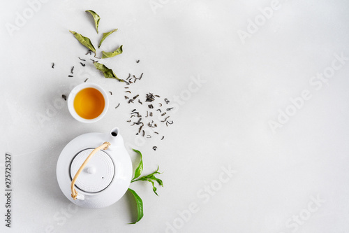 Obraz na plátně Tea concept with white tea set of cups and teapot surrounded with fresh tea leaves on concrete background with copy space