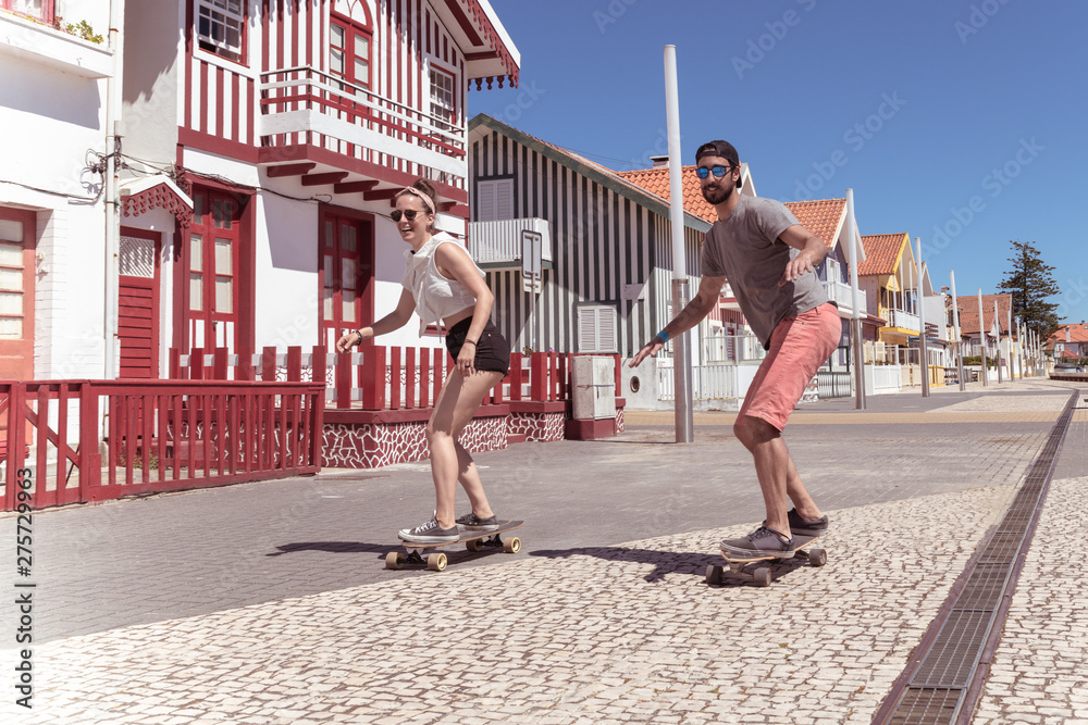 Young active couple enjoying a summer sunny day skateboarding - obrazy, fototapety, plakaty 