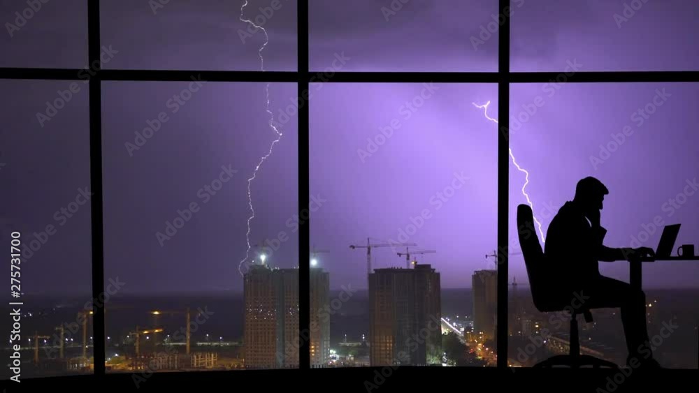The man working near a panoramic window on a city with lightning background