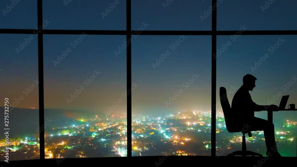 The man working near a window on a night city background. time lapse