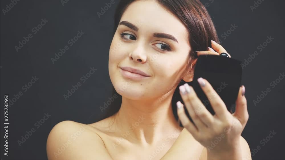 Close up portrait young gorgeous girl looking in mirror and holding makeup brushes in right hand. Close up portrait young gorgeous girl looking in mirror and holding makeup brushes in right hand.