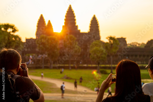 Photographer at Angkor Wat temple in Siem Reap, Cambodia. Smartphone photo and people walking. Sunrise behind the three towers. Hindu temple.