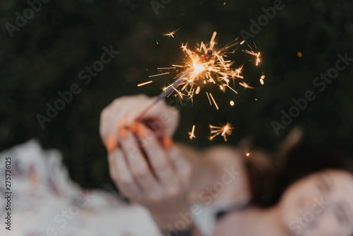 A woman in her twenties with tattoos holding a sparkler in the summer