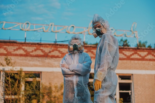 Two scientists put on a respirator and a radiation protective suit. Stern look into the camera from the abandoned territory. Care about ecology in bright saturated photos.