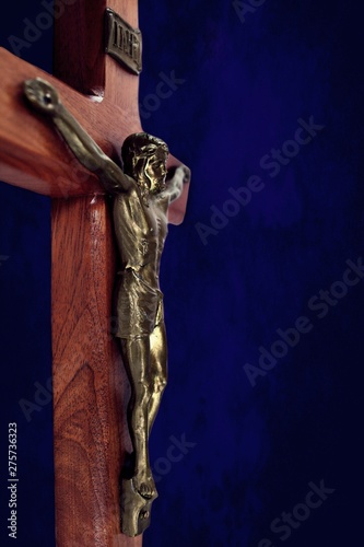 Profile of wood crucifix with gold body of Jesus isolated on dark blue background