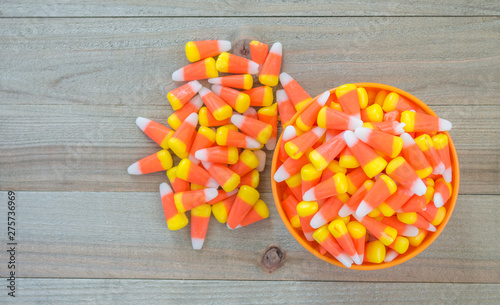 small orange bowl overflowing with colorful candy corn on a wood background viewed from above with copy space