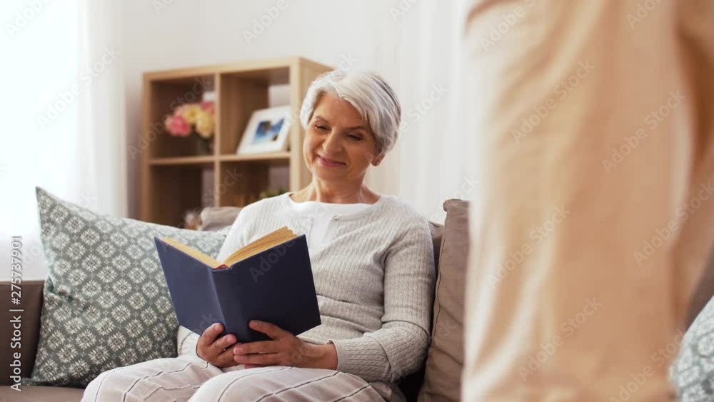 family, generation and people concept - happy smiling adult son bringing coffee to senior mother reading book at home family, generation and people concept - happy smiling adult son bringing coffee to senior mother reading book at home