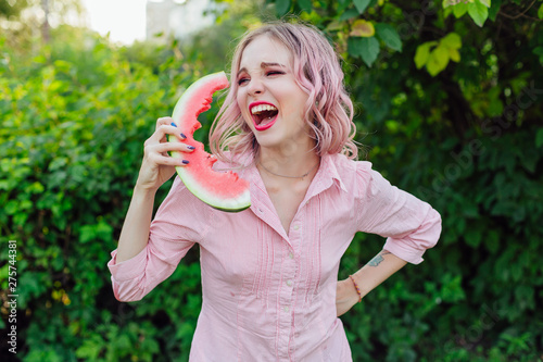 Beautiful emotional young woman with pink hair holding watermelon like telephone