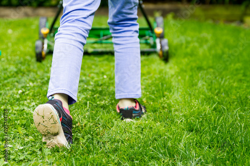 Person pushing a reel mower across the lawn, feet in focus; young person cutting fresh green grass with reel mower