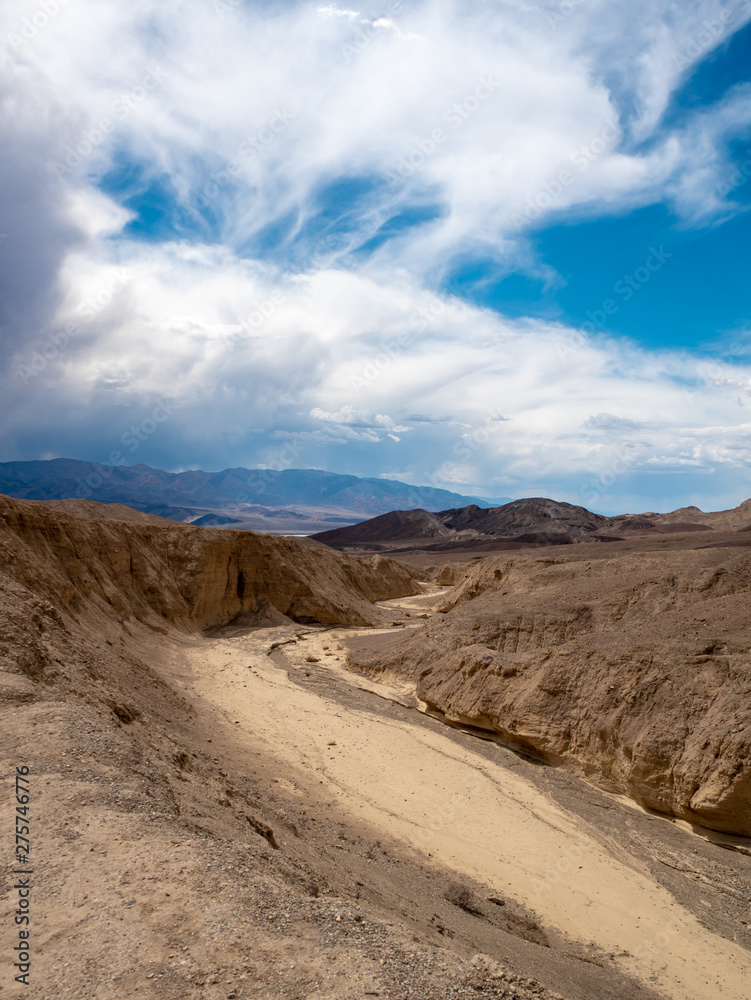 Water erosion formed wash (ravine) and approaching rain storm in Death Valley National Park, vertical orientation.