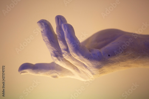 Detail of a white marble Sculpted male hand in yellow and purple light