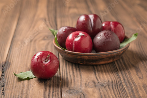 Ripe plums in a bowl and on a wooden table.