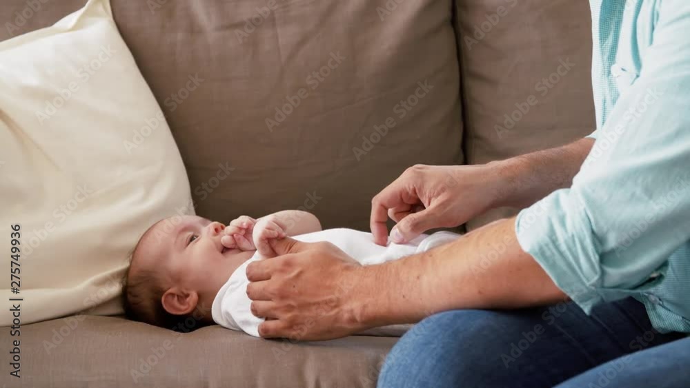 family, parenthood and fatherhood concept - middle aged father playing with little baby daughter lying on sofa at home family, parenthood and fatherhood concept - middle aged father playing with little baby daughter lying on sofa at home