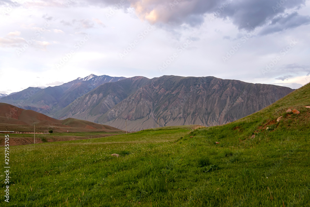 Sunset in the mountains of Tien Shan. Pastures on the background of snow-capped peaks of the mountain range.