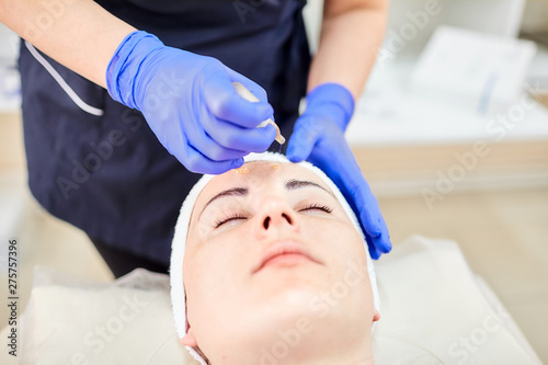 Cosmetologist hands in gloves. Skincare. Beautician drips a cosmetic product on the face of a woman. Beauty procedure. Facial treatment.