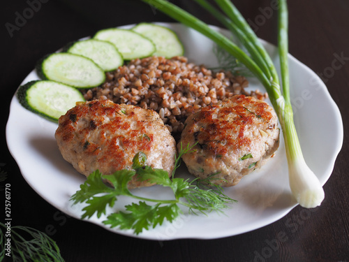  Cutlets with vegetables and garnish are in a white plate on a dark table.  photo