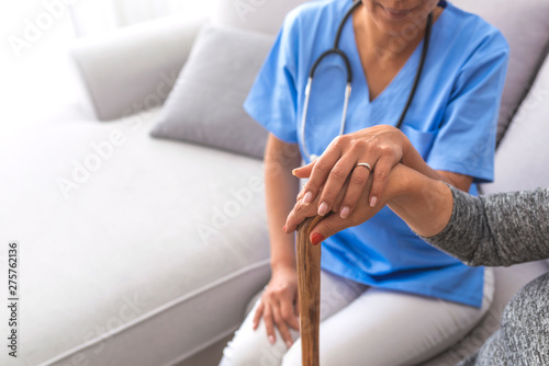 Close-up of elderly woman holding walking stick in the nursing house. Closeup of senior lady holding walking stick in one hand and holding nurse's hand. Young carer supporting senior disabled woman © Dragana Gordic