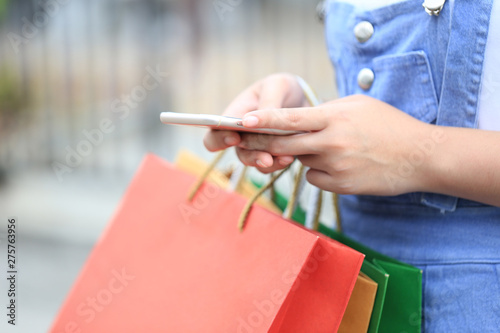 Closeup of young woman hand holding smartphone and shopping bags with standing at the car parking lot