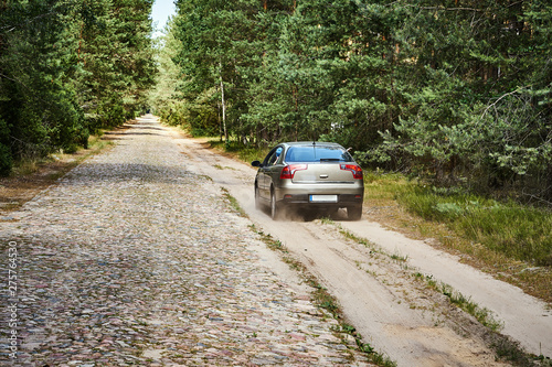 bright car is driving along a gravel road in the forest