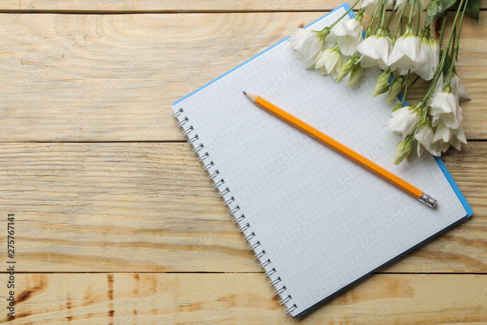 Notebook with a pencil and white flowers on a natural wooden table. top view Notebook with a pencil and white flowers on a natural wooden table. top view