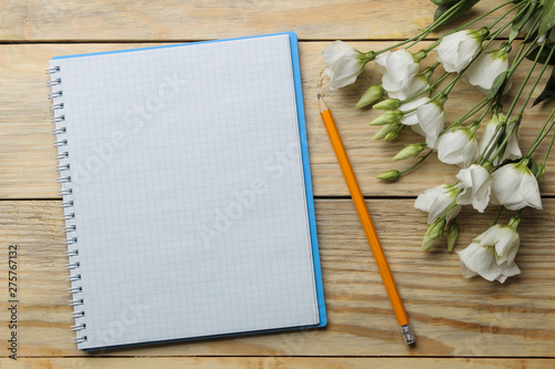 Notebook with a pencil and white flowers on a natural wooden table. top view