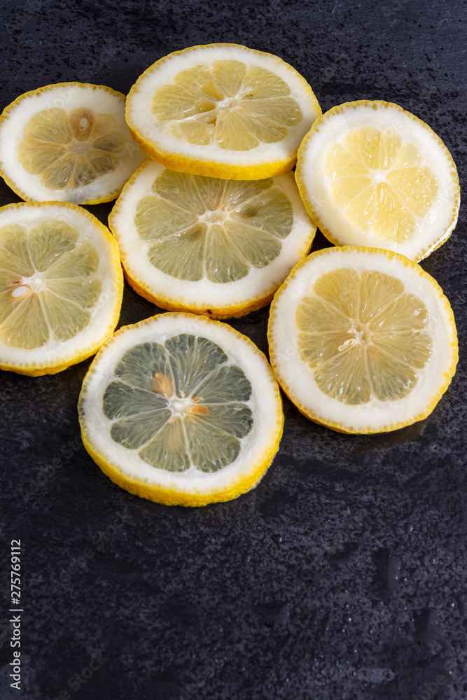 Top view of slices of lemon on wet black stone background in vertical Top view of slices of lemon on wet black stone background in vertical