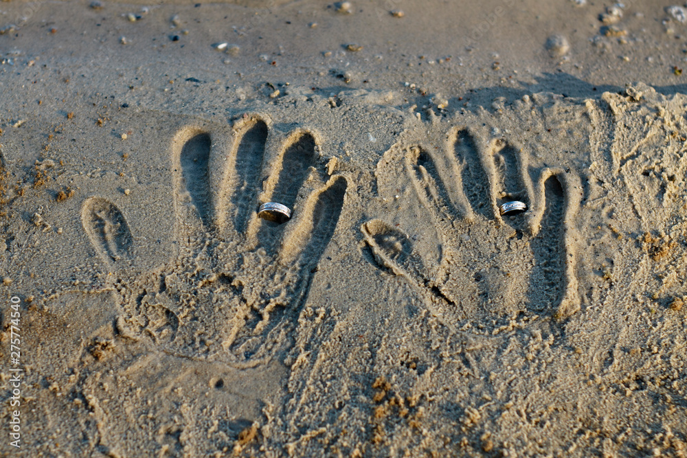 Fototapeta premium Newlyweds wear rings. Wedding ceremony. Handprints in the sand. Bride and groom with rings.