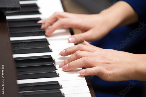 Closeup of the hands of a young woman playing the piano. The girl musician is preparing to start playing a musical composition. Synthesizer or classical piano with classic keys. Music concept