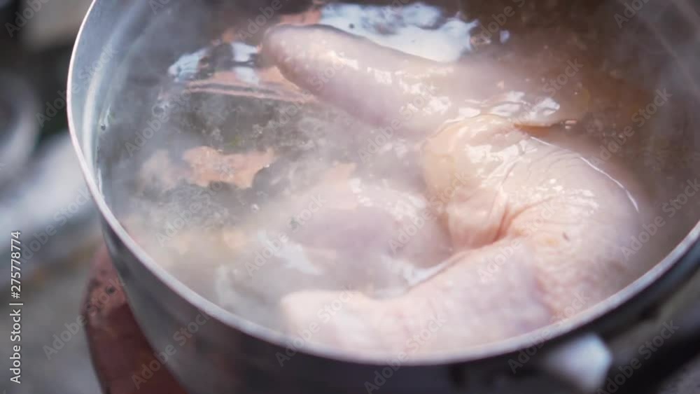 Old lady add another chicken thigh to a boil soup pot.