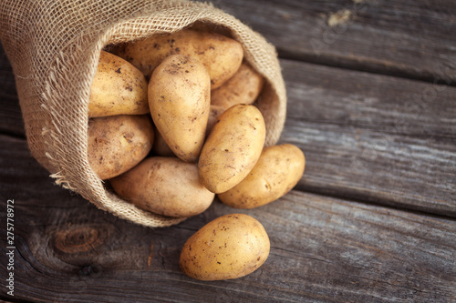 Raw potato food . Fresh potatoes in an old sack on wooden background