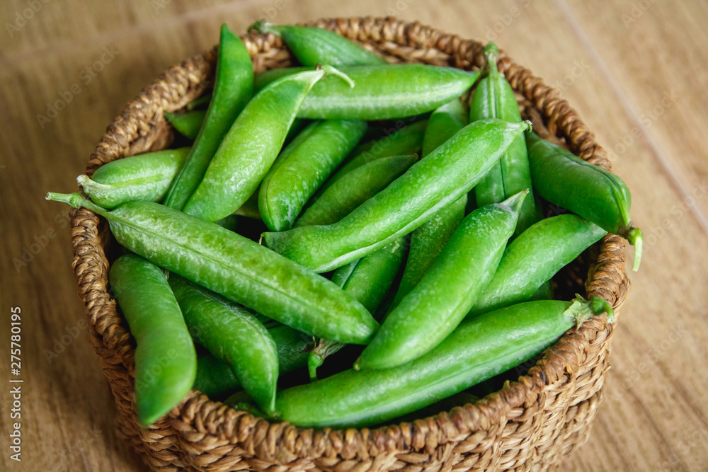 The crop of peas lies in a round wicker basket on a wooden background. Close up. The crop of peas lies in a round wicker basket on a wooden background. Close up.