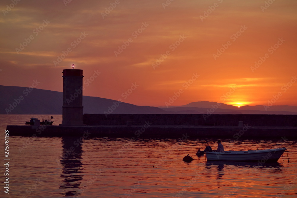 Sunset in Town of Senj, Primorje, Croatia. In the background lighthouse and fisherman in the boat.