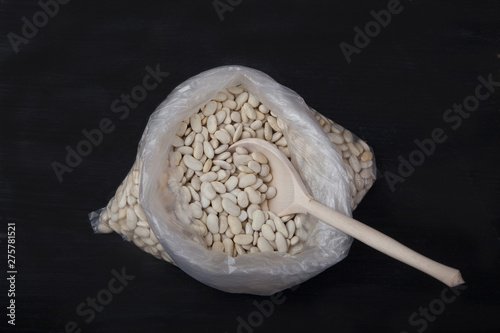 white beans and wooden spoon in a plastic bag on a black background. Trend. Plasicfree photo