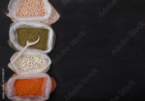 White beans, red lentils, peas and mung bean in plastic bags on a black background photo