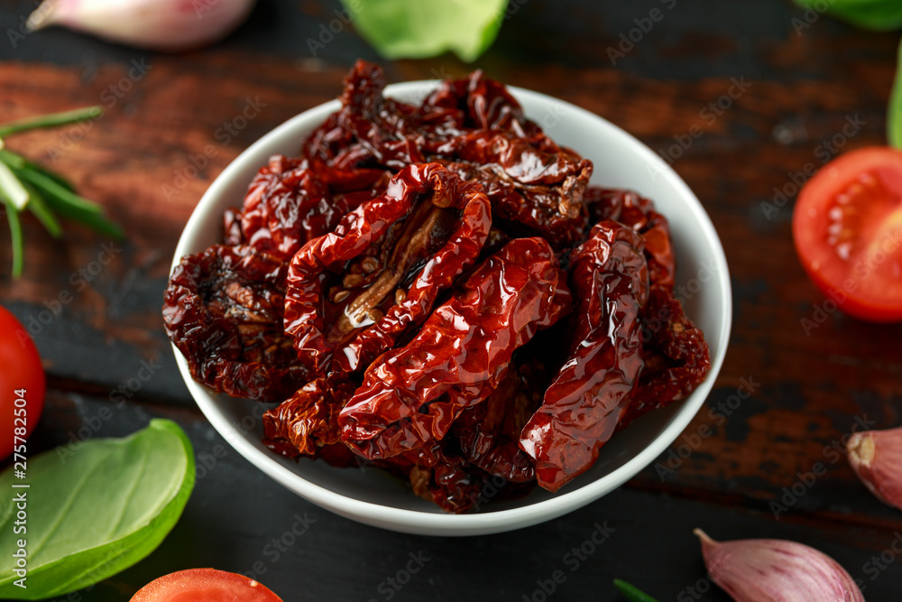 Sun dried tomatoes in white bowl with fresh herbs and spices on wooden table Sun dried tomatoes in white bowl with fresh herbs and spices on wooden table