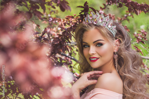 Beautiful woman with queen crown in pink dress with red lips and make up outside