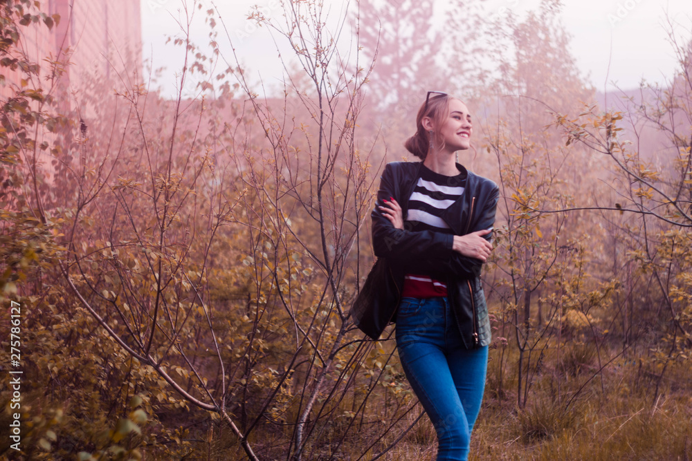 Naklejka premium Blonde in striped jacket against brick building and trees in pink smoke