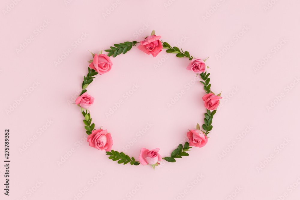 Floral wreath made of pink roses and green branches on a pink background.