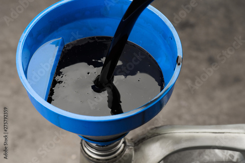 Pouring old black oil of  car engine from oil pan into bottle on top view lubrication used for recycle