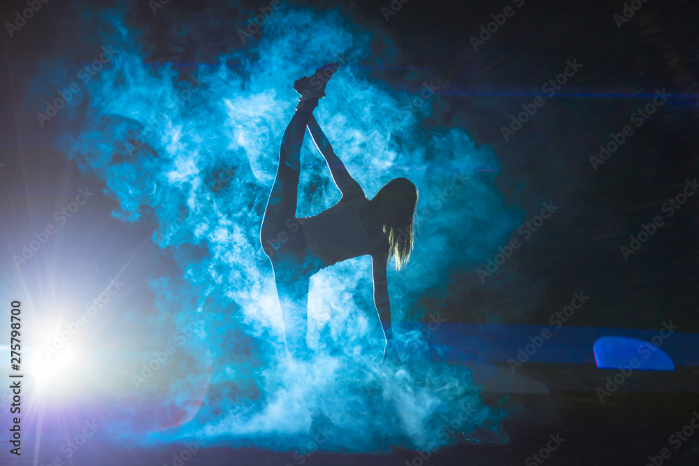 The woman doing vertical split in the smoke on a dark background