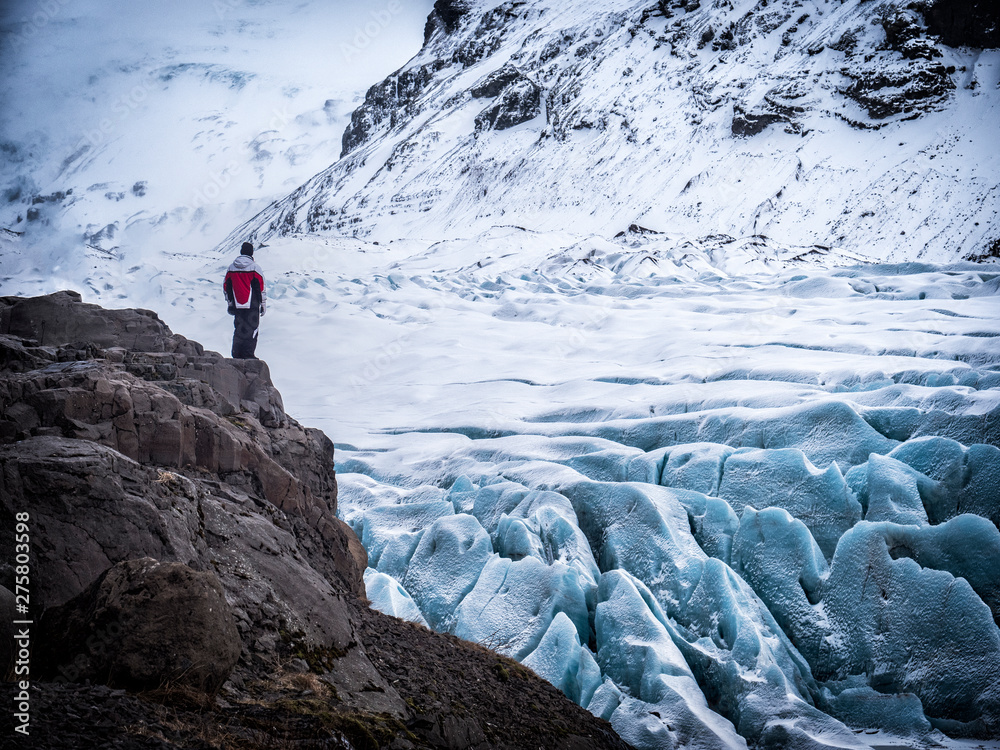 Back view of professional mountaineer in warm clothes walking on icy surface glacier by snowy mountain in Iceland