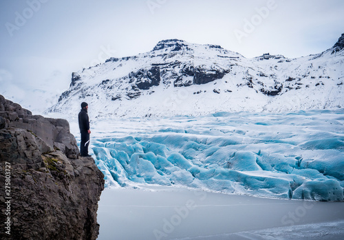 Back view of professional mountaineer in warm clothes walking on icy surface glacier by snowy mountain in Iceland