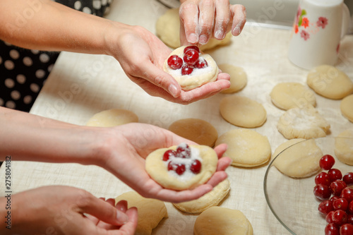 Cooking cherry pies in the home kitchen. Women's hands in the process of cooking cakes with cherries.