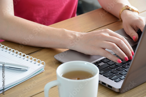 Young woman with a neat pink manicure using modern laptop. With cup of tea and notebook. 