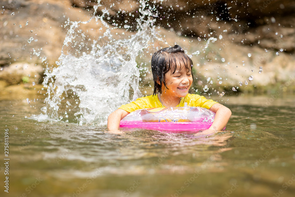 Obraz premium Asian girl in pool ring playing water in stream, Little female kid with pool ring kicking water splash, Water activity