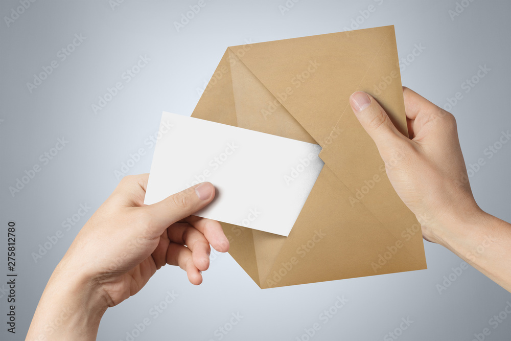 Hands pulling a blank sheet of paper (letter, ticket, flyer, invitation, coupon, banknote, etc.) out a brown envelope on gray background
